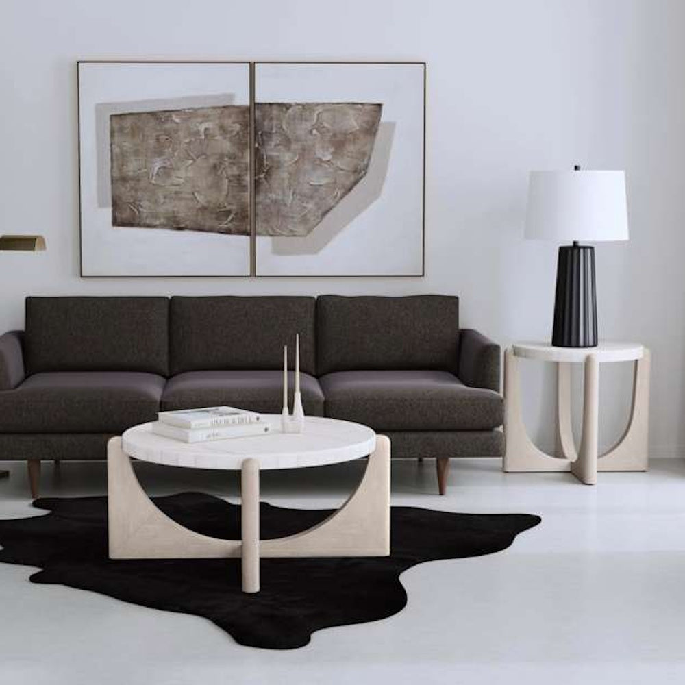 Modern living room with dark gray sofa, round marble coffee table, and abstract wall art.