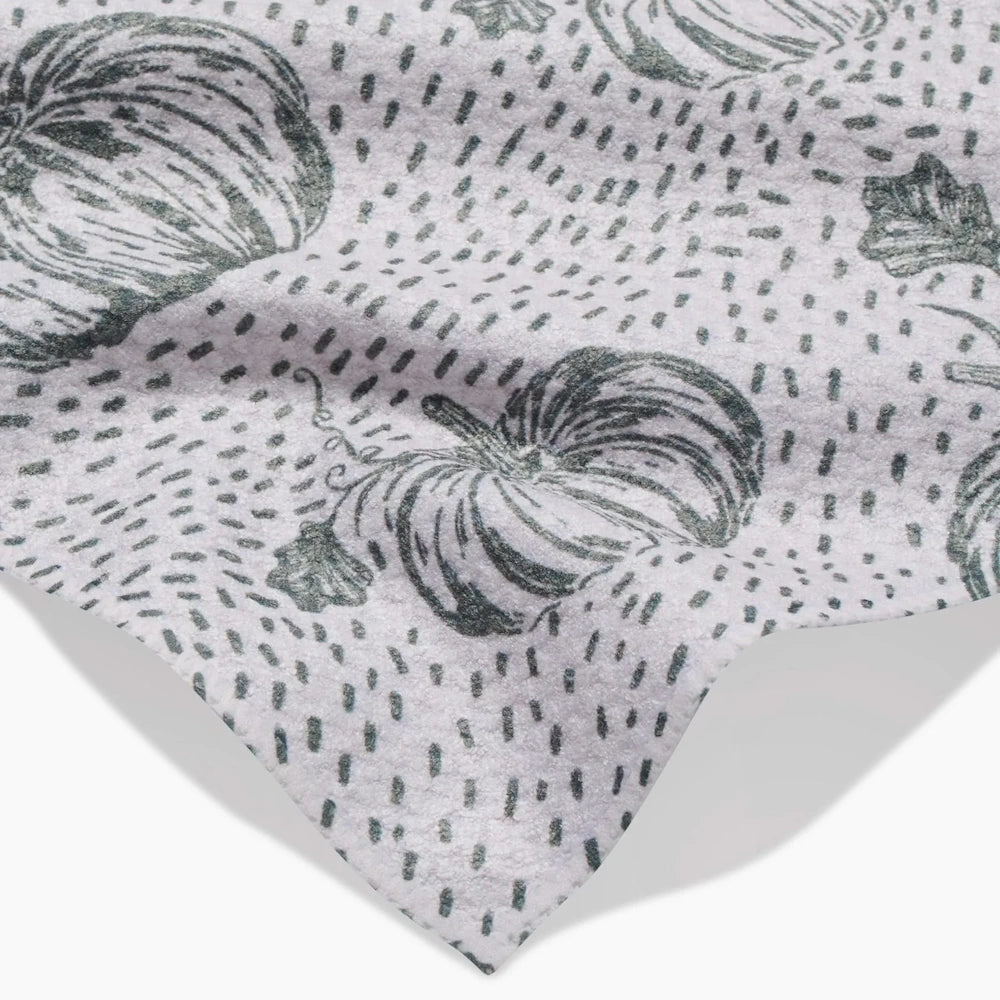 Close-up of a white fabric towel with a green sketched pumpkin pattern and small dashed lines.