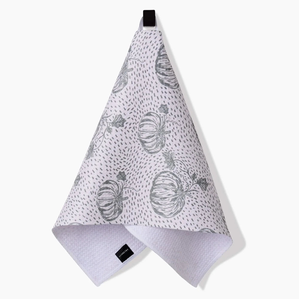 A hanging white kitchen towel with a waffle texture features a pattern of sage green sketched pumpkins.