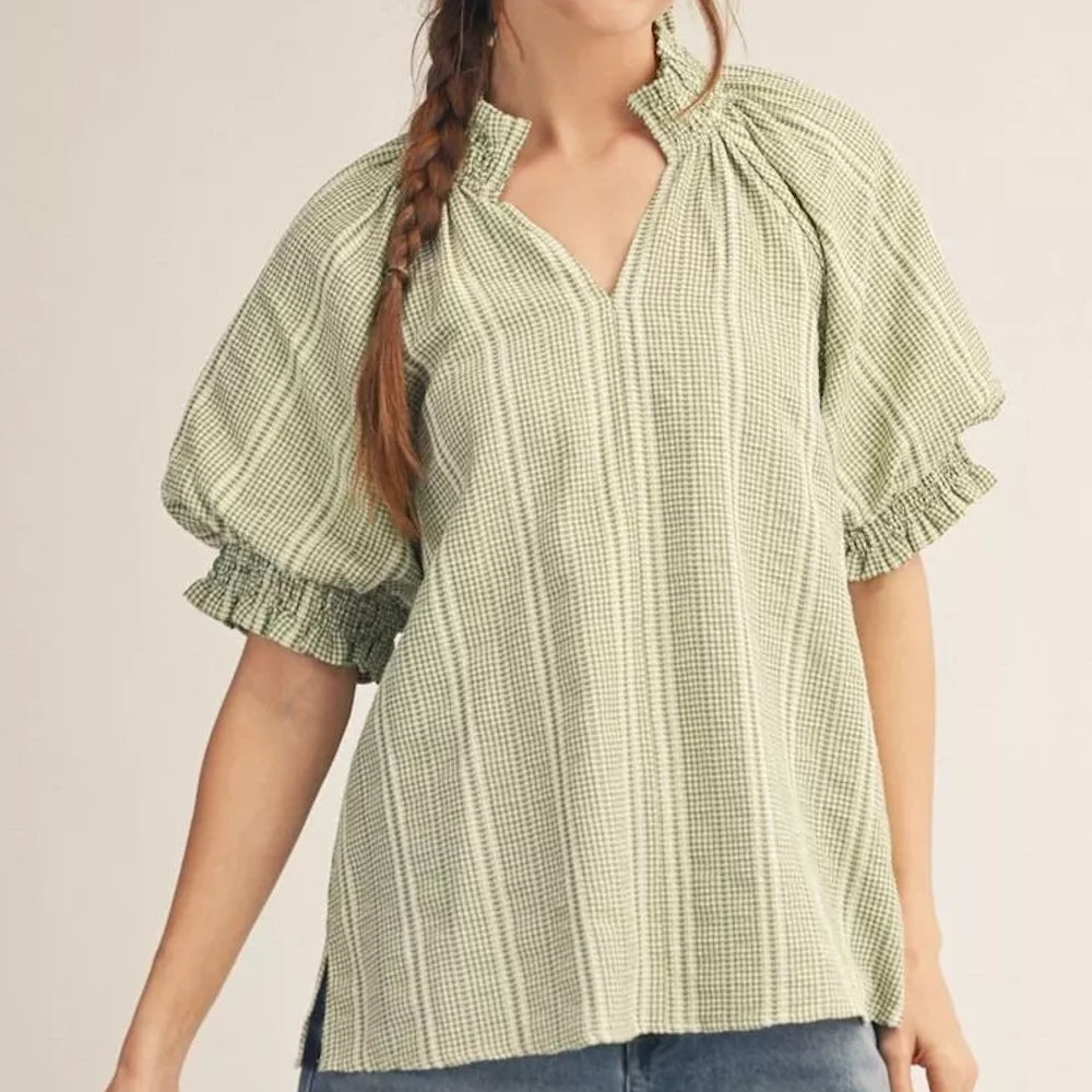 A woman wearing a green and white checkered blouse with puff sleeves and a ruffled neckline.