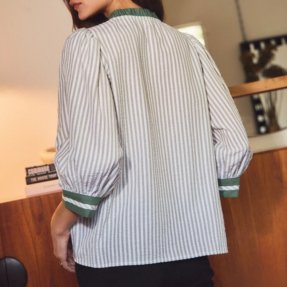 Woman from behind wearing a sage green and white vertical striped blouse with puffy sleeves and green cuffs.