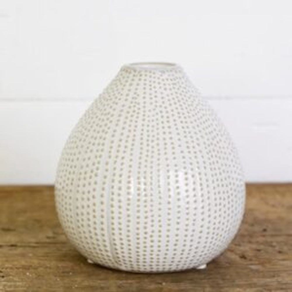 A teardrop-shaped white ceramic vase with a textured beige dotted pattern on a wooden surface.