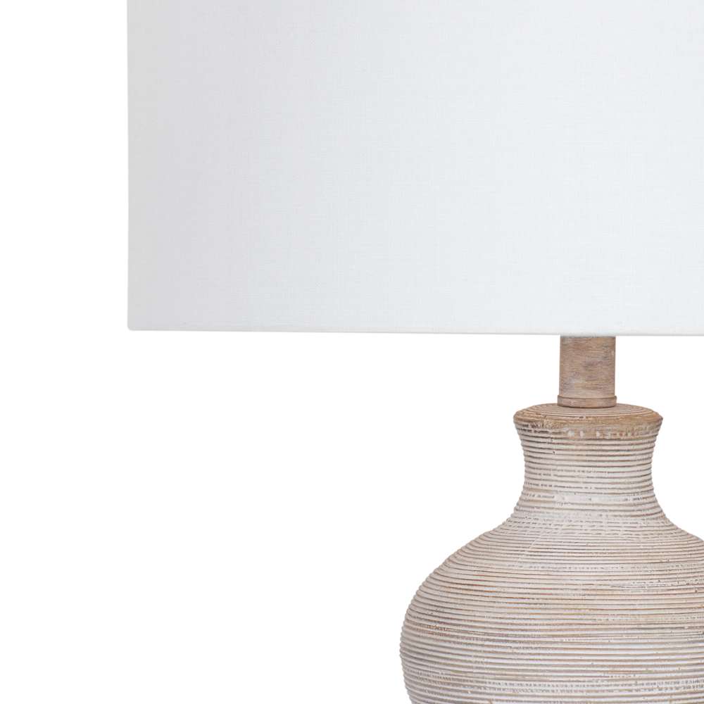 Close-up of a rustic, textured ceramic table lamp with a ribbed off-white base and a white drum shade.