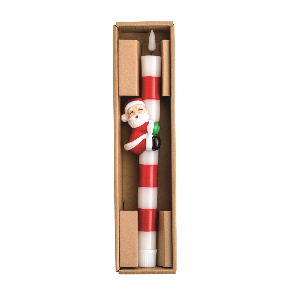 Top-down view of a red and white striped wax taper candle set in a cardboard box, featuring a Santa figurine hugging the candle shaft.
