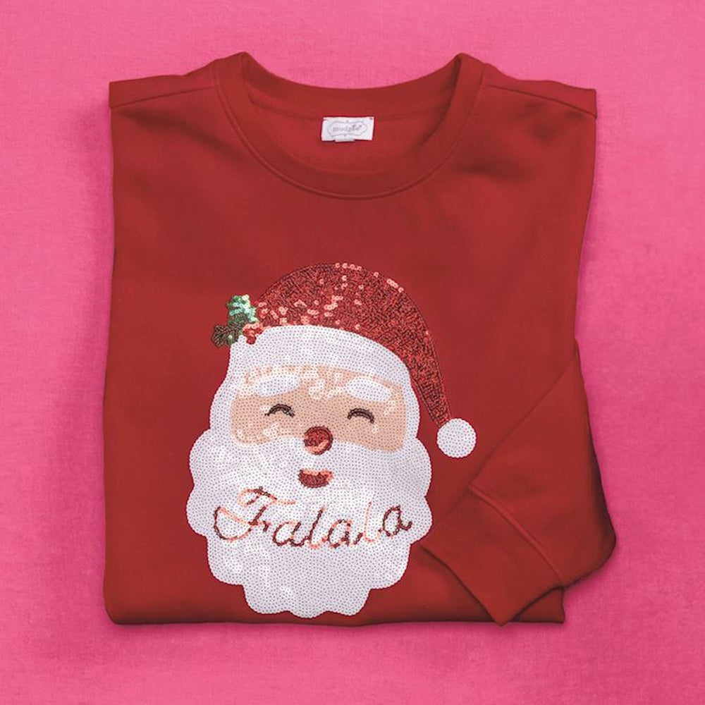 Folded red sweatshirt with a sequined Santa Claus face and "Fa la la" written on his beard.