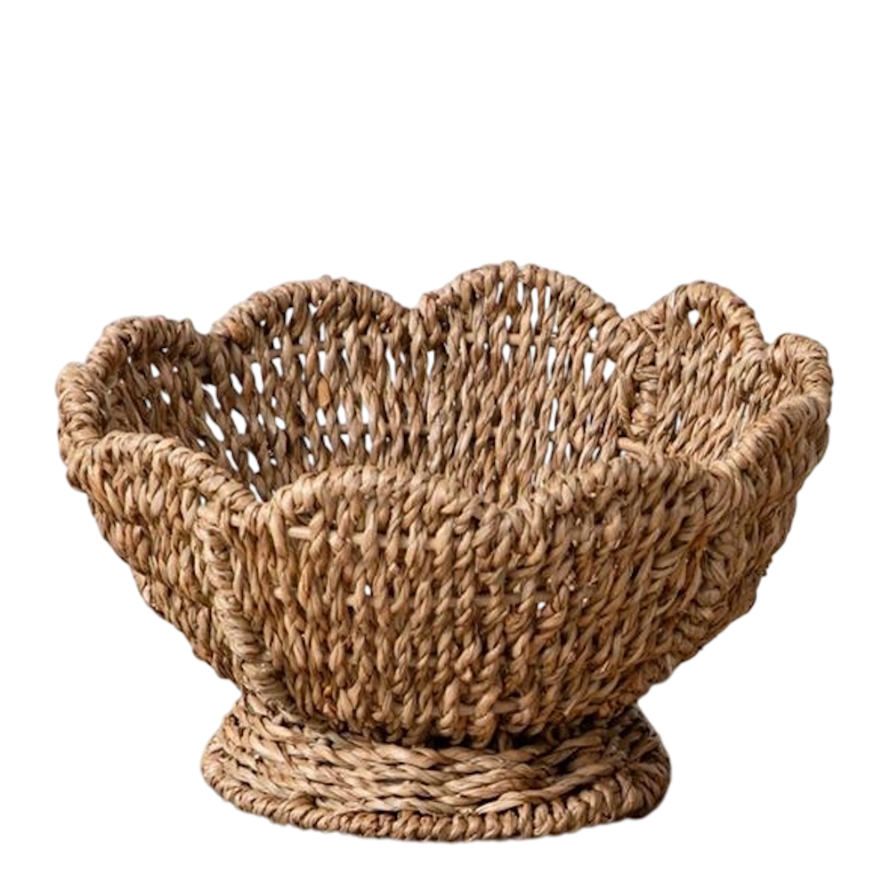 Woven seagrass basket with a scalloped rim and footed base on a white background.