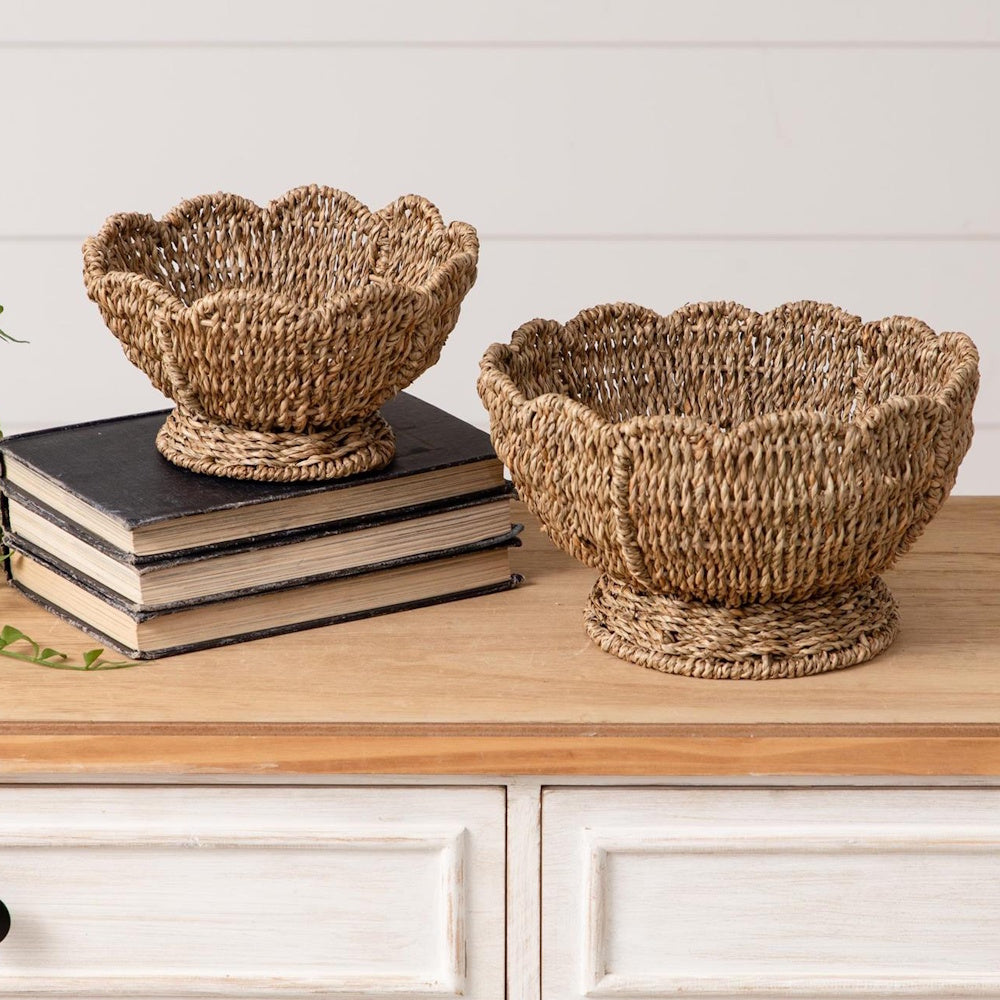 Two scalloped woven seagrass bowls on a wooden dresser, one resting on a stack of three vintage books.