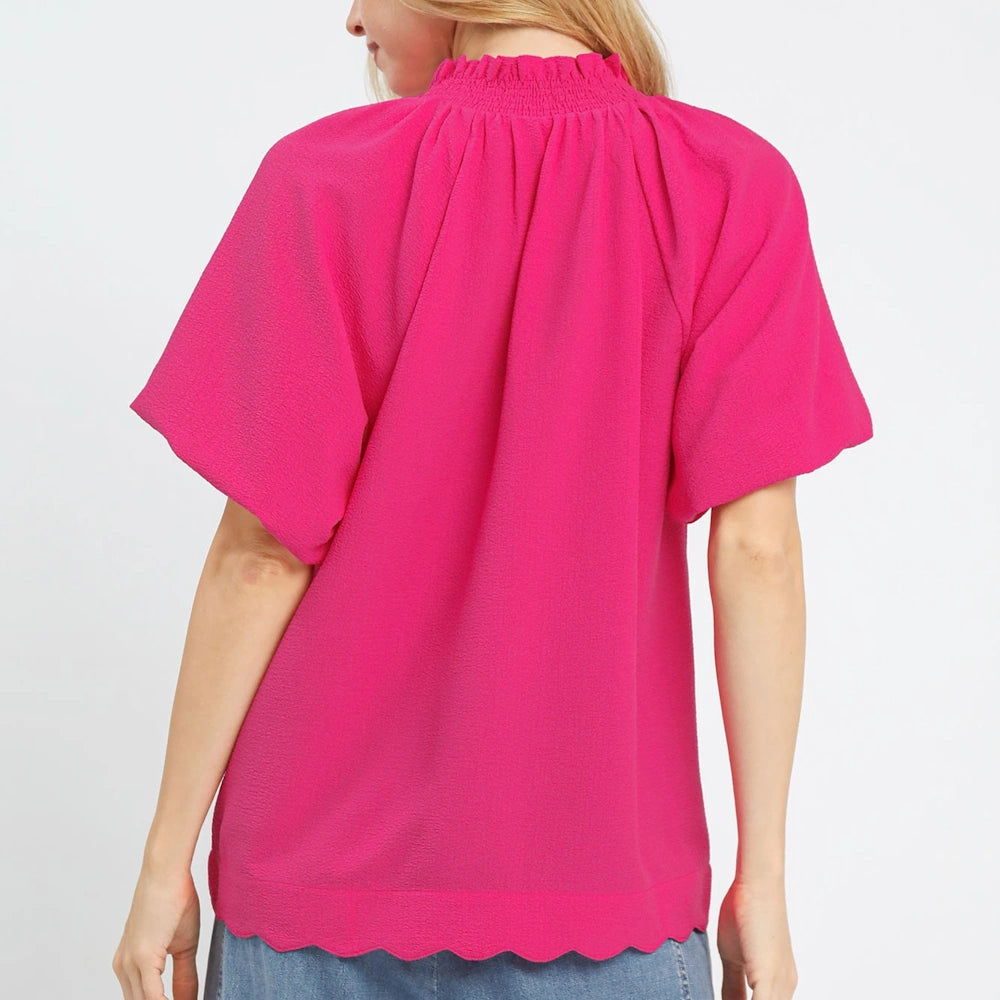 Back view of a hot pink textured blouse featuring a ruffled high neck, flutter sleeves, and a scalloped hem.