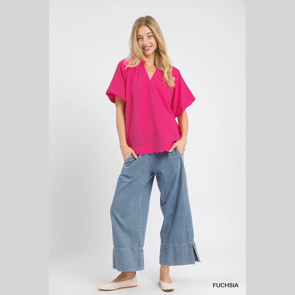Fuchsia textured short-sleeve blouse with a scalloped hem and V-neck, paired with wide-leg denim jeans and cream flats.