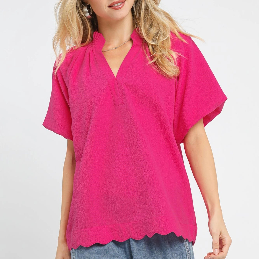 Woman in a hot pink textured blouse with a V-neck, short flutter sleeves, and a scalloped hem over blue jeans.
