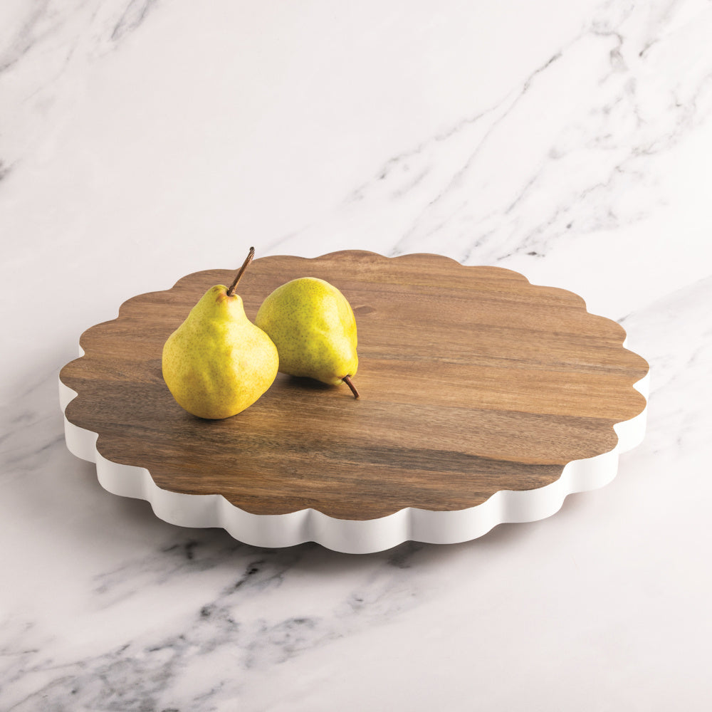 Scalloped wood lazy susan with white trim and two yellow pears on a marble countertop.