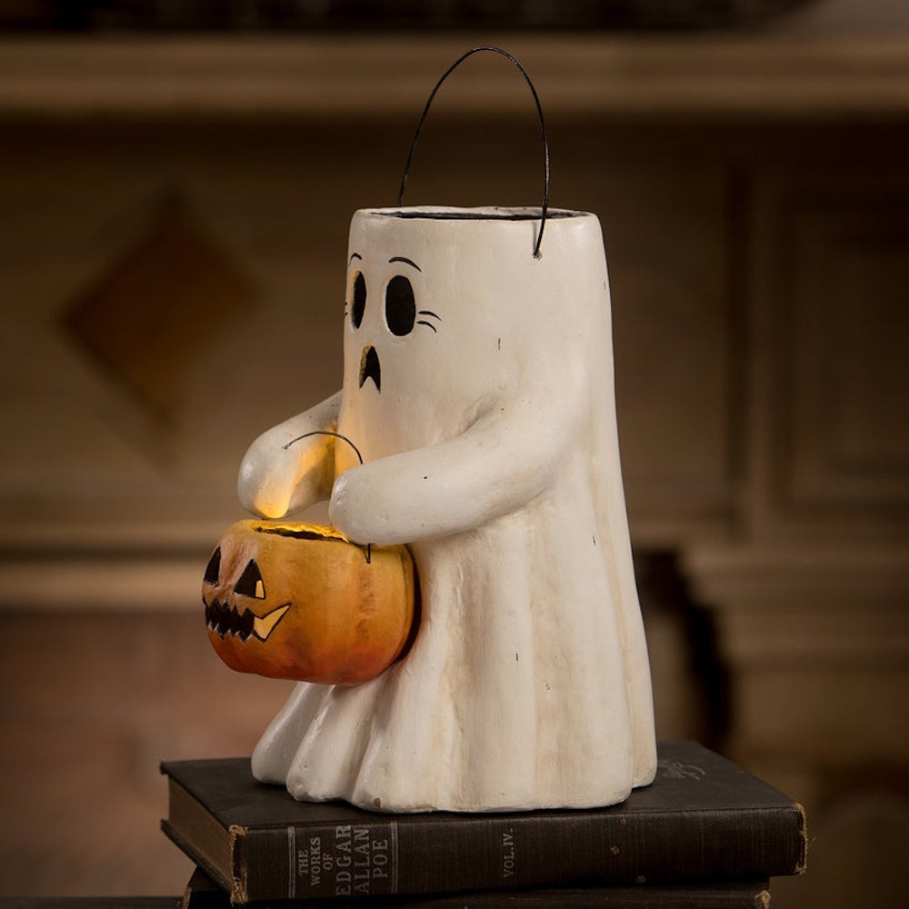 Side profile of an illuminated ghost lantern holding a jack-o'-lantern bucket on stacked books.