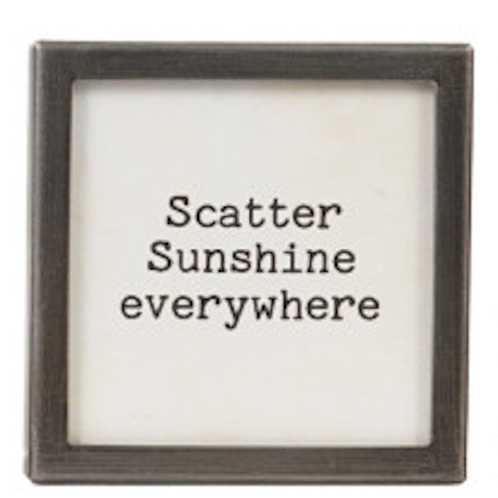 A square silver-framed sign with the text "Scatter Sunshine everywhere" in black typewriter font.