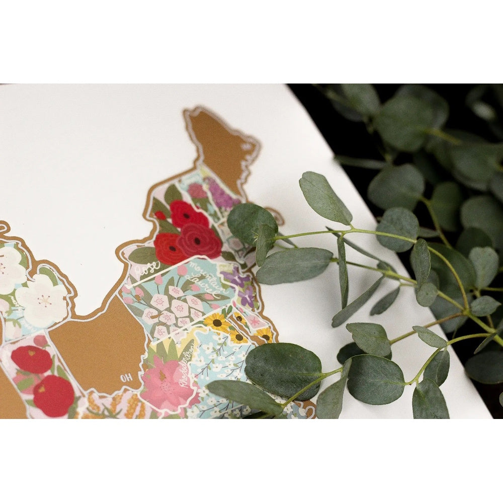 Close-up of a scratch-off USA travel map featuring colorful floral illustrations of state flowers on a white base.