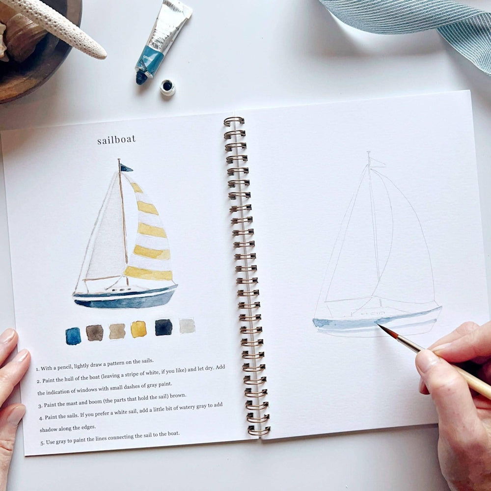 Watercolor sailboat workbook page showing step-by-step painting instructions with a hand holding a brush.