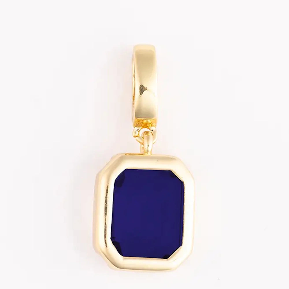 Gold pendant charm featuring an emerald-cut deep blue gemstone set in a thick gold bezel.