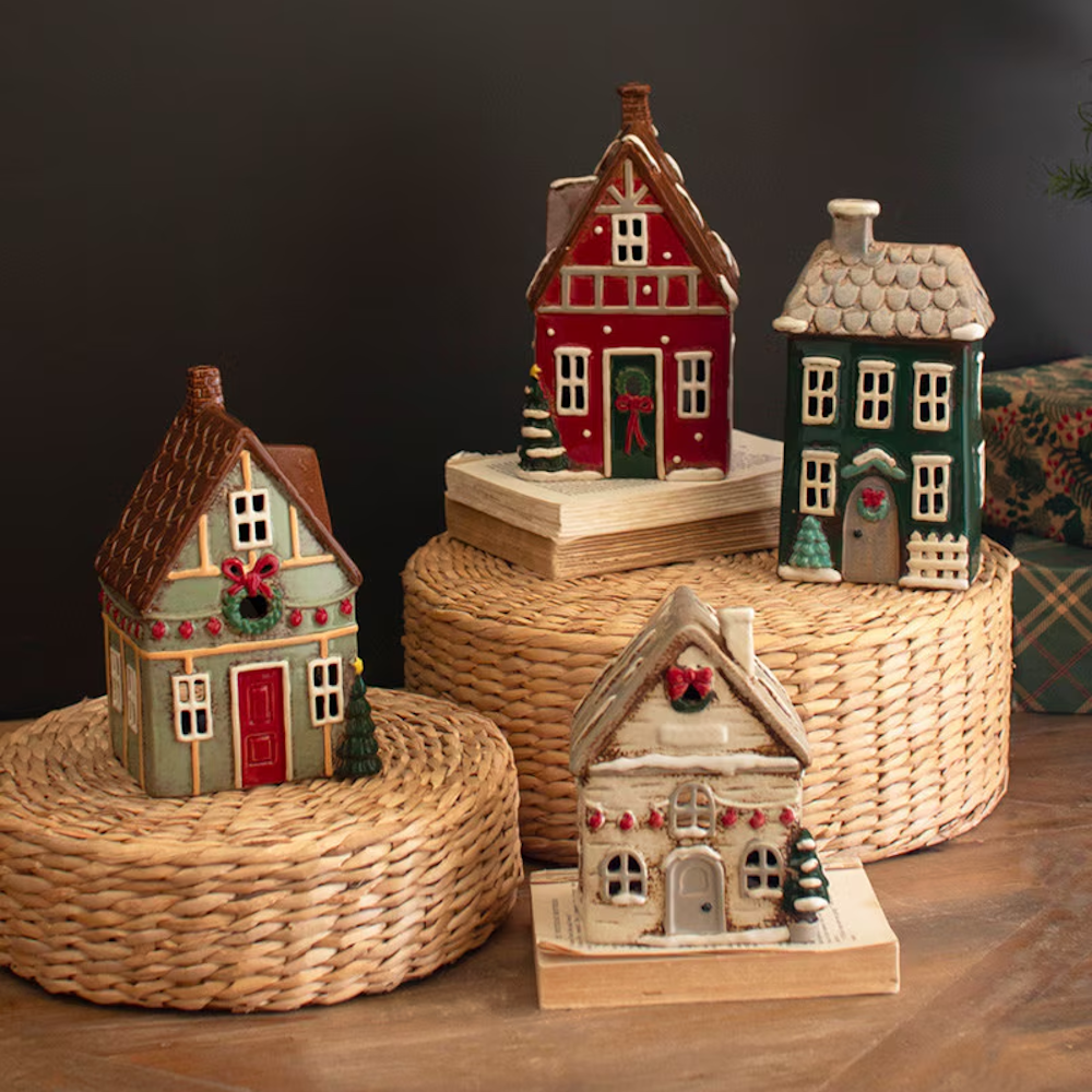 Set of four ceramic Christmas village houses displayed on woven risers and books.