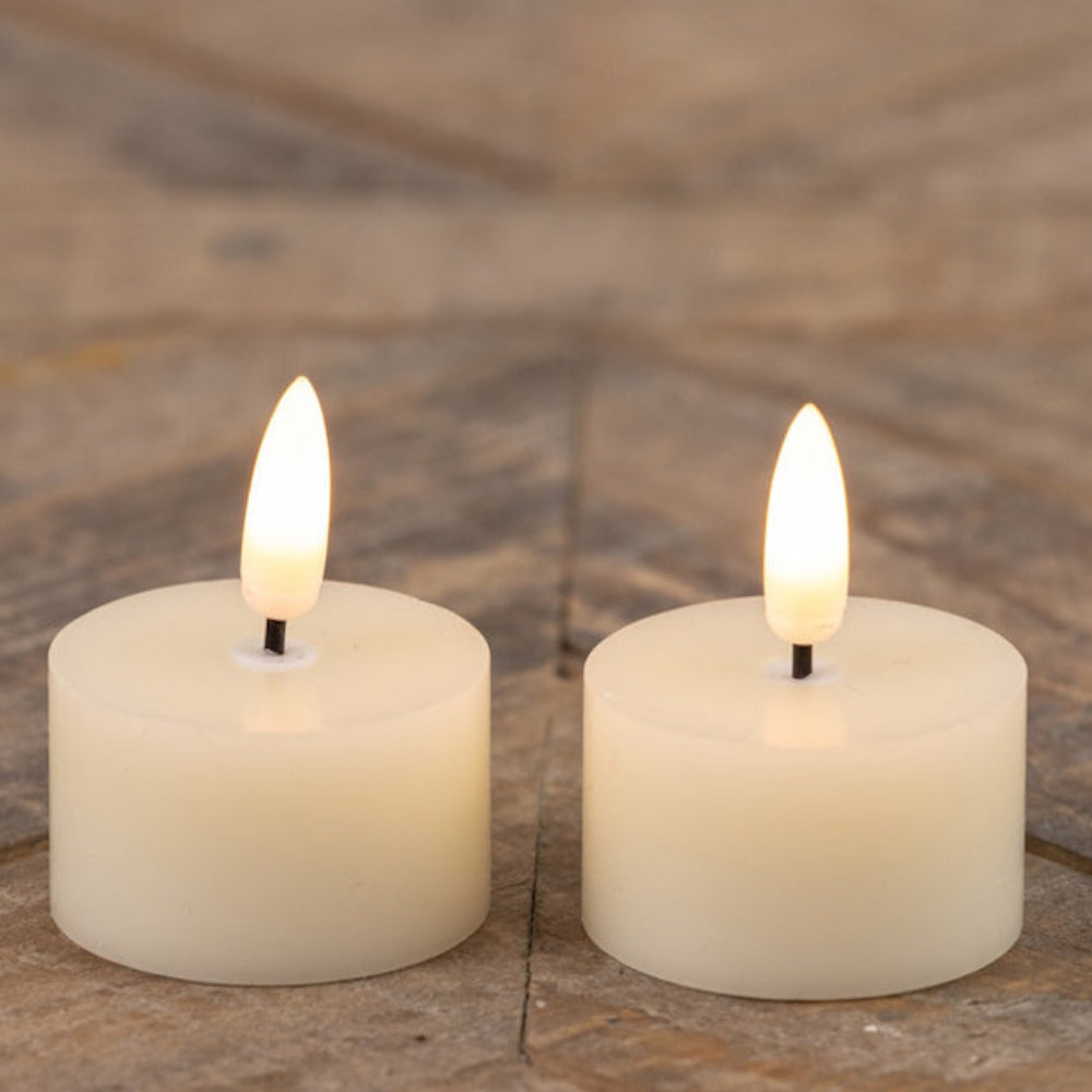 Two lit cream-colored flameless tea light candles resting side by side on a patterned wooden surface.
