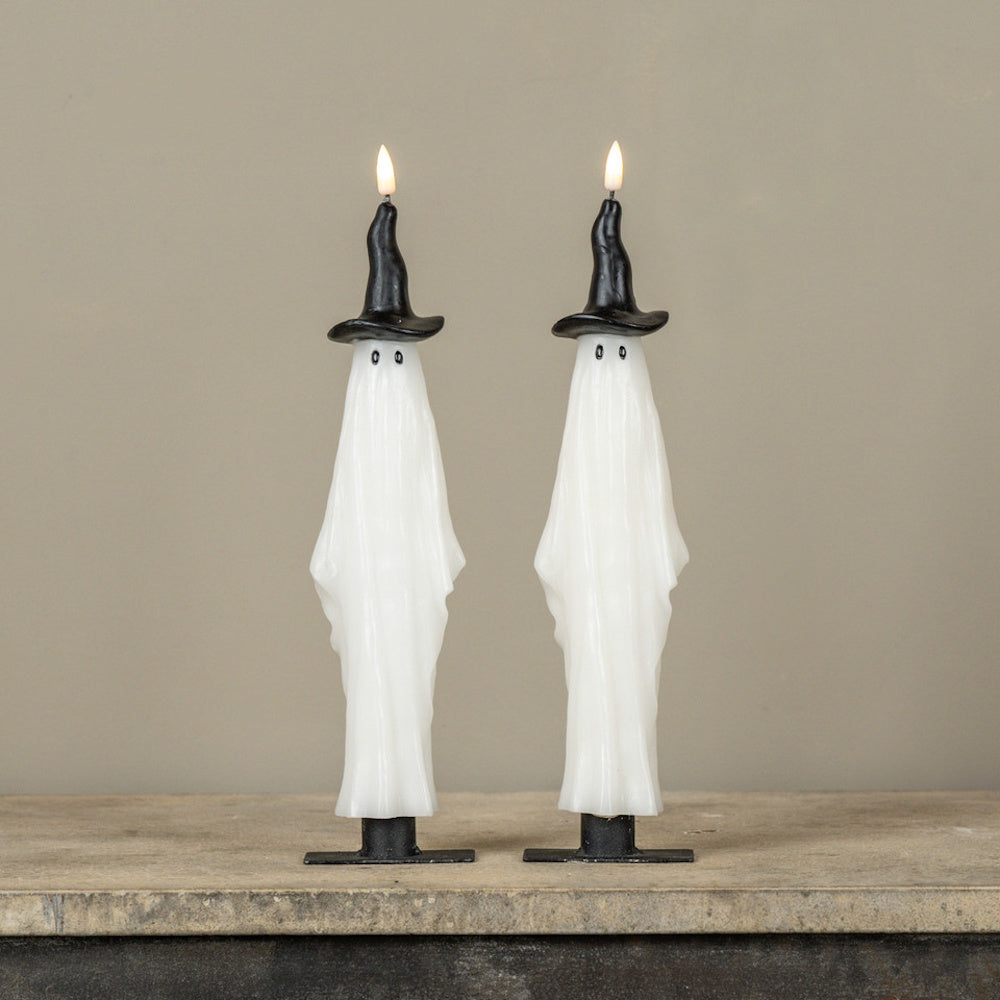 Two lit ghost taper candles wearing black witch hats standing side by side on a stone surface.