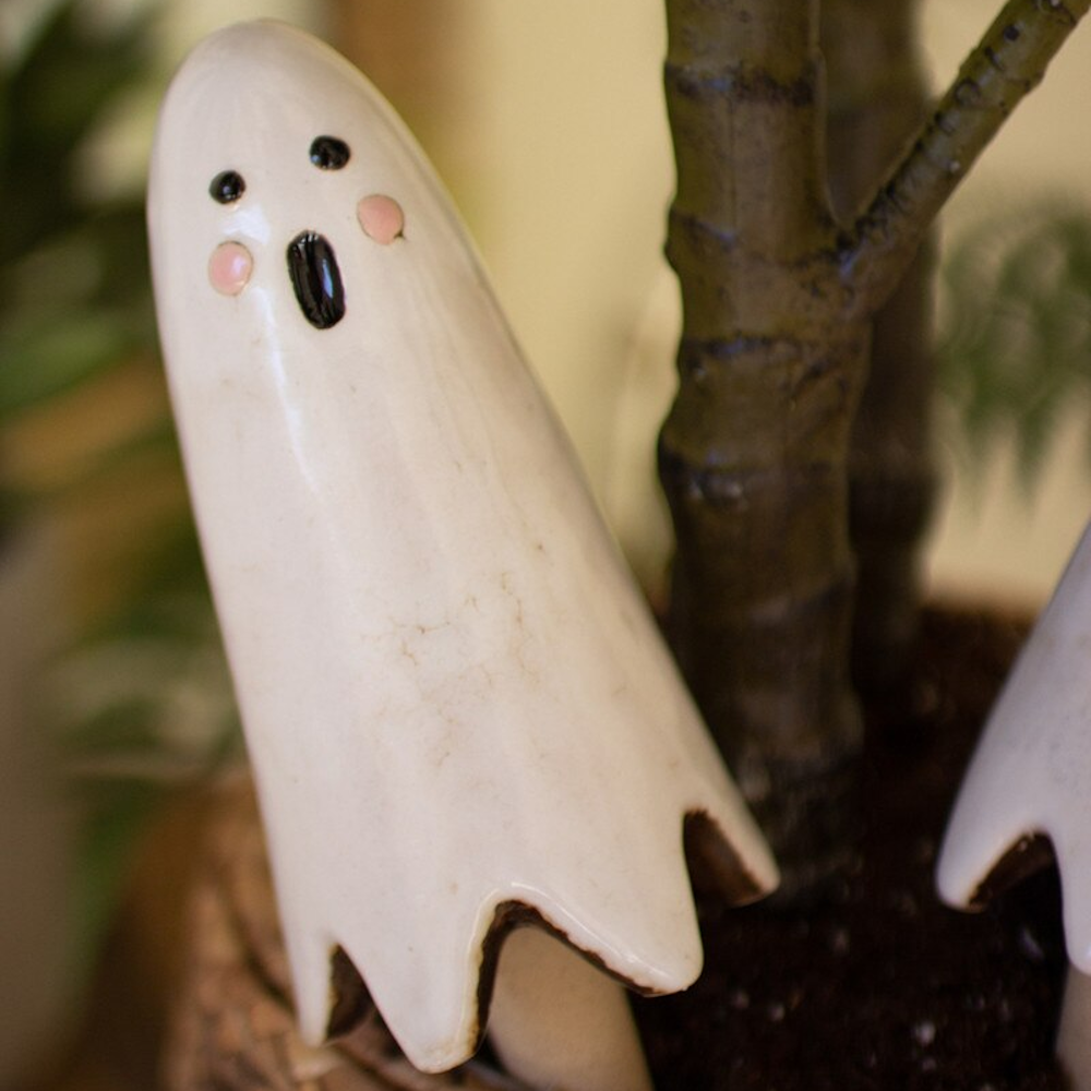 Cute white ceramic ghost plant stake with pink cheeks next to a houseplant.