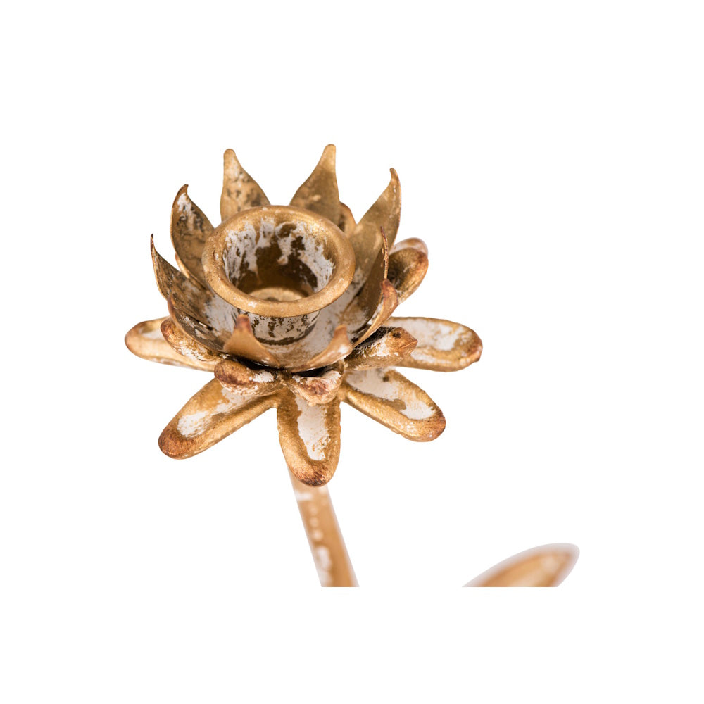A close-up of a gold metal taper candle holder shaped like a layered flower with a white distressed finish.