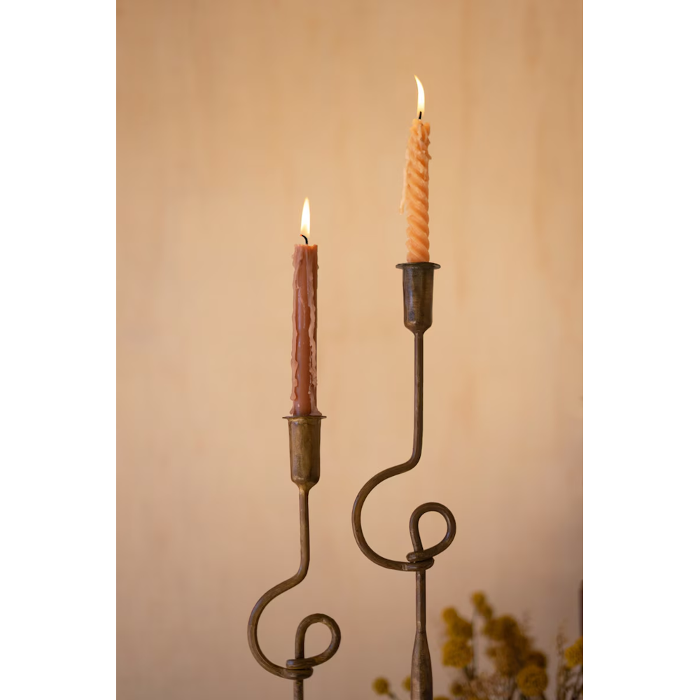 Close-up of lit taper candles in antique brass forged iron holders with decorative looped stems.