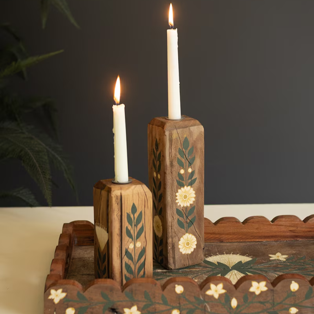 Two hand-painted wooden block candle holders with floral designs and lit white taper candles.