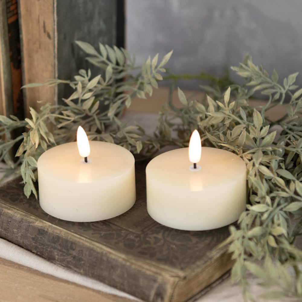 Two cream flameless tealights glowing on an antique book with greenery.