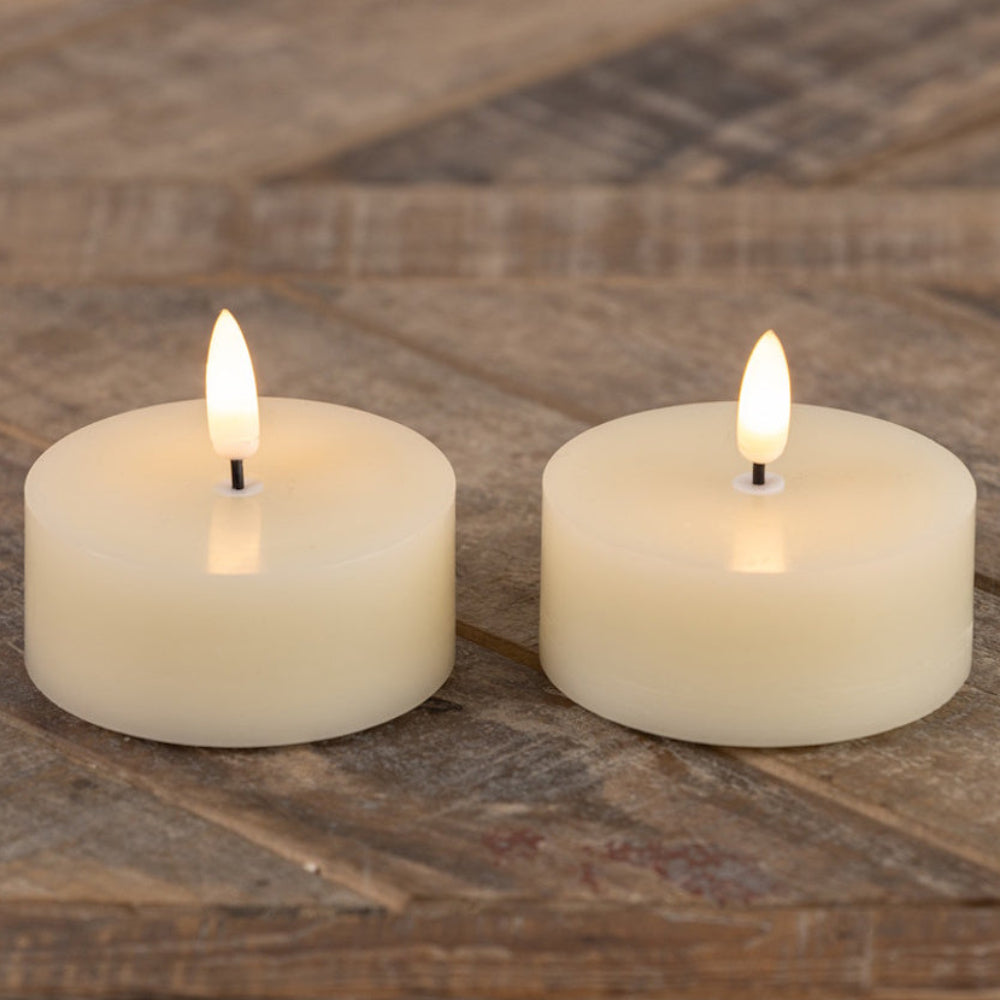 Two glowing cream-colored oversized tea light candles resting on a rustic wooden surface.