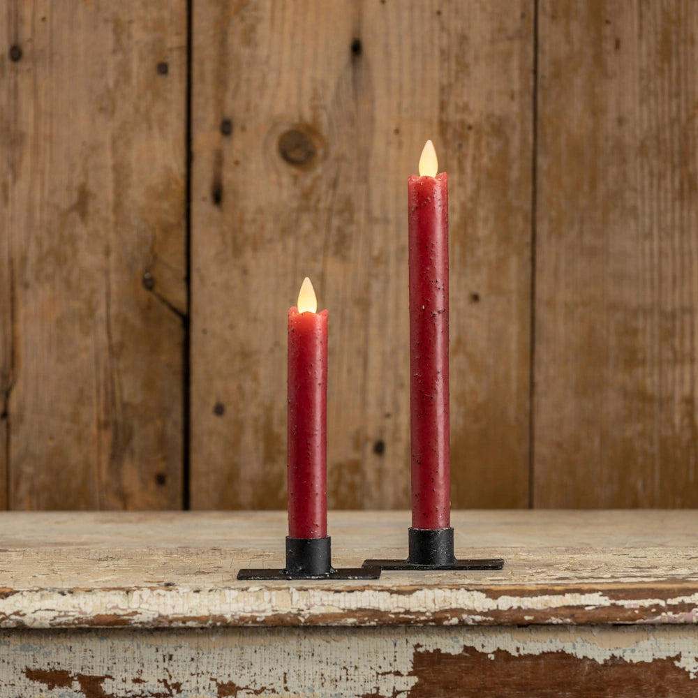 Two red flameless taper candles in black holders against a rustic wooden wall background.