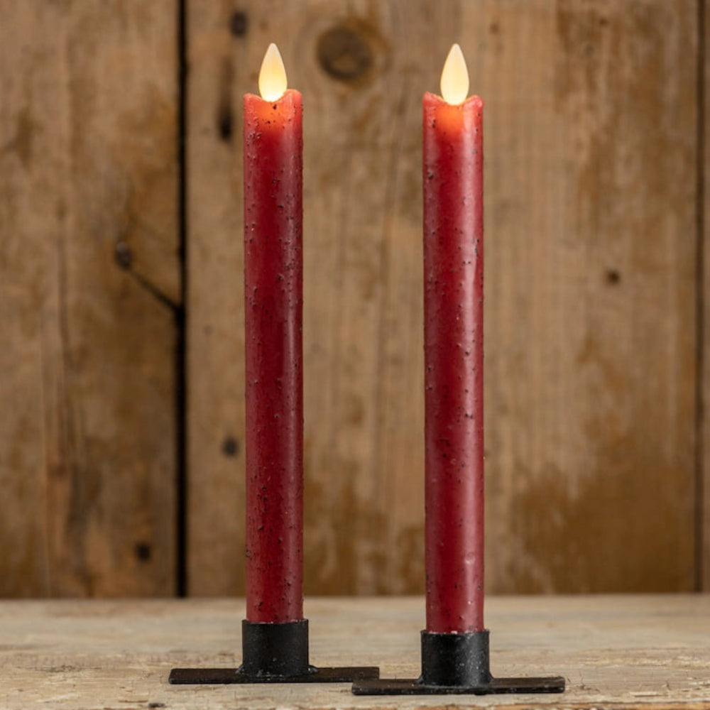 Two lit rustic red taper candles standing in black holders on a weathered wooden ledge.