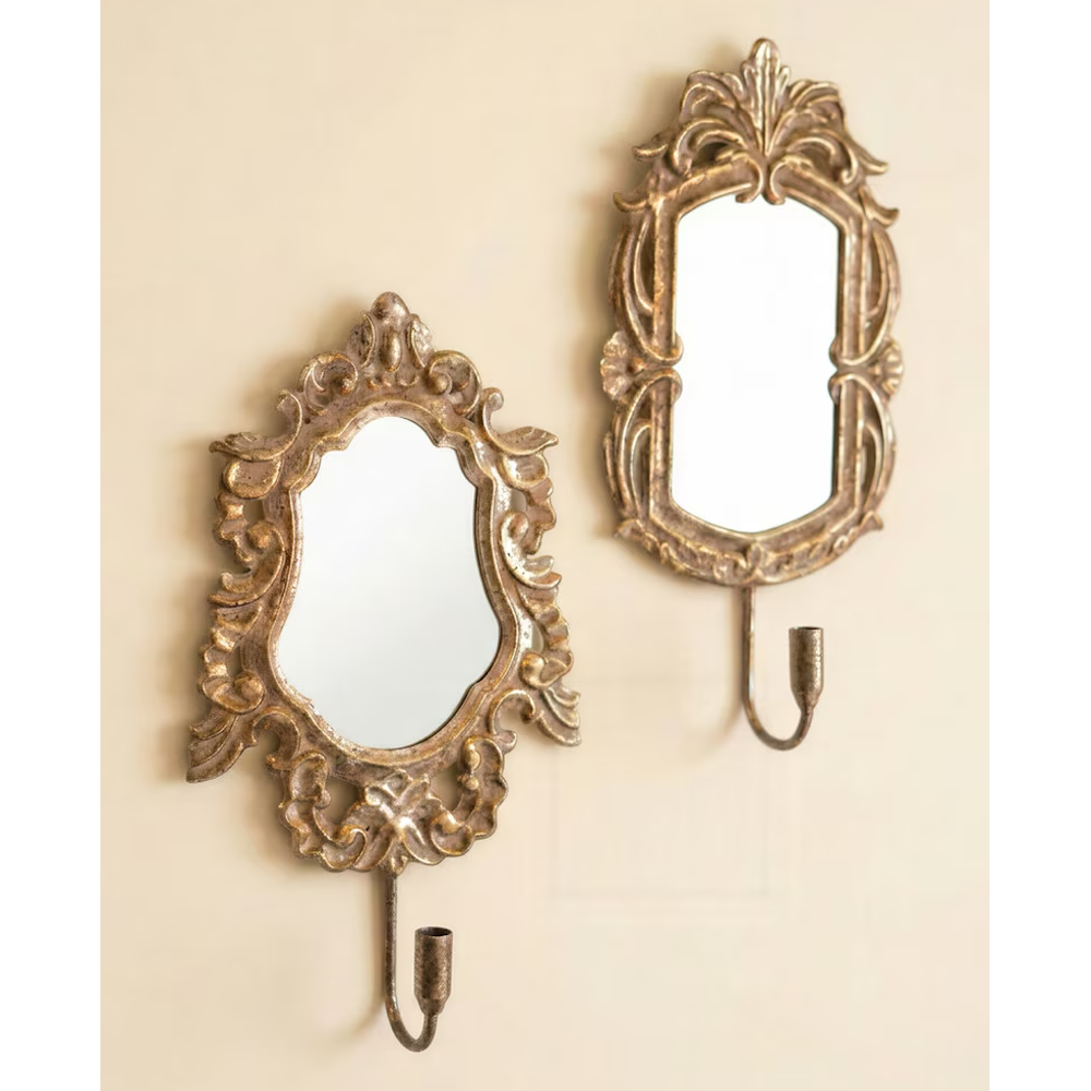 Set of two ornate antique gold mirror sconces with taper candleholders on a beige wall.