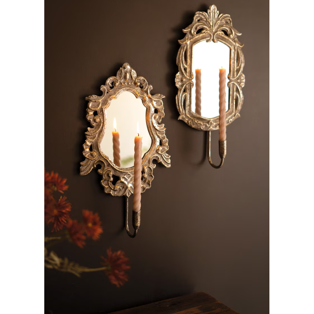Ornate antique gold framed mirror sconces holding glowing taper candles against a dark wall.