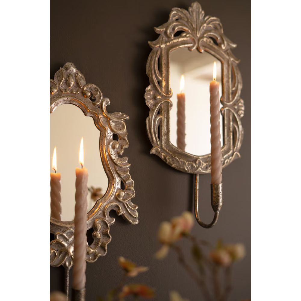 Close-up view of antique gold mirror sconces with glowing spiral taper candles against a dark wall.