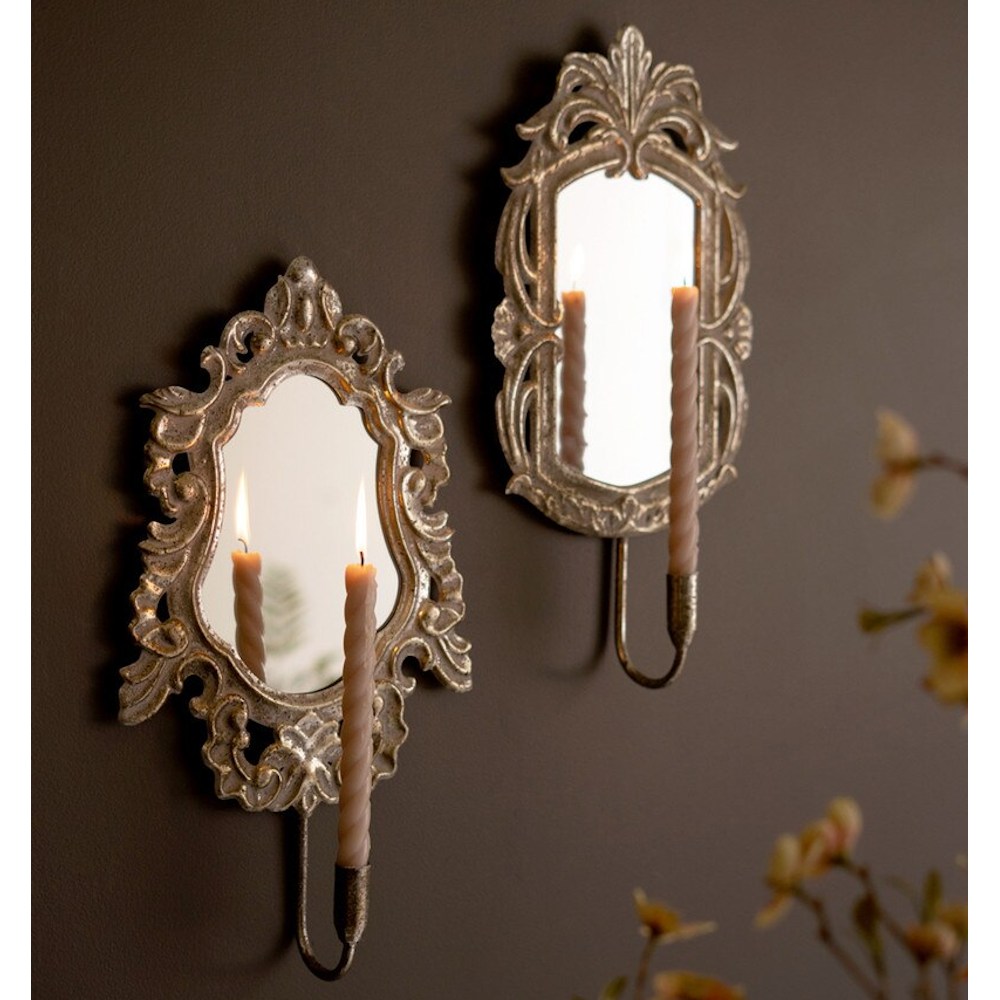 Pair of vintage-inspired ornate gold mirror wall sconces holding lit spiral taper candles.