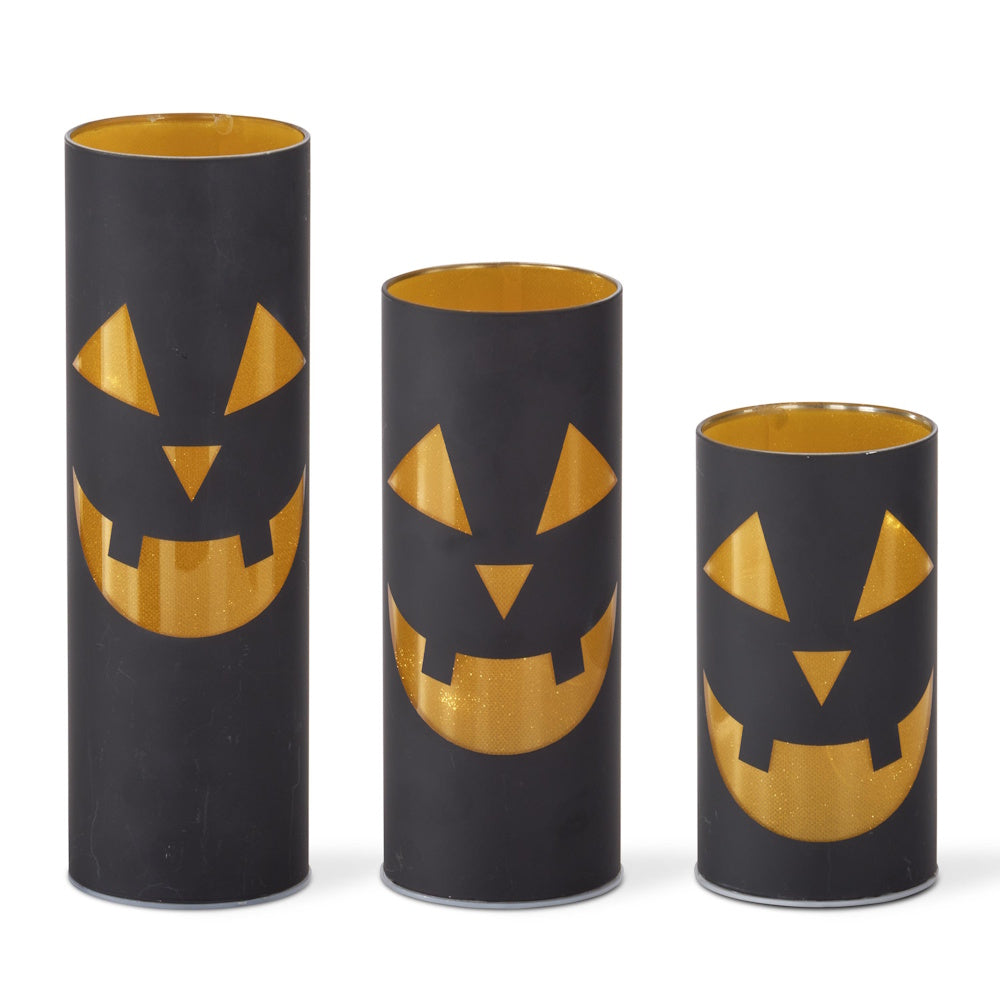 Set of three black and gold laser-engraved jack-o'-lantern LED cylinder lanterns in varying heights.