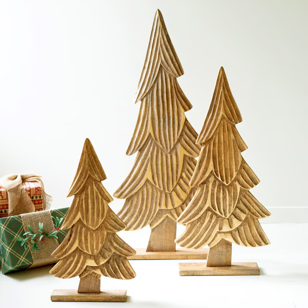 Set of 3 carved natural mango wood Christmas trees with subtle gold details next to wrapped gifts.