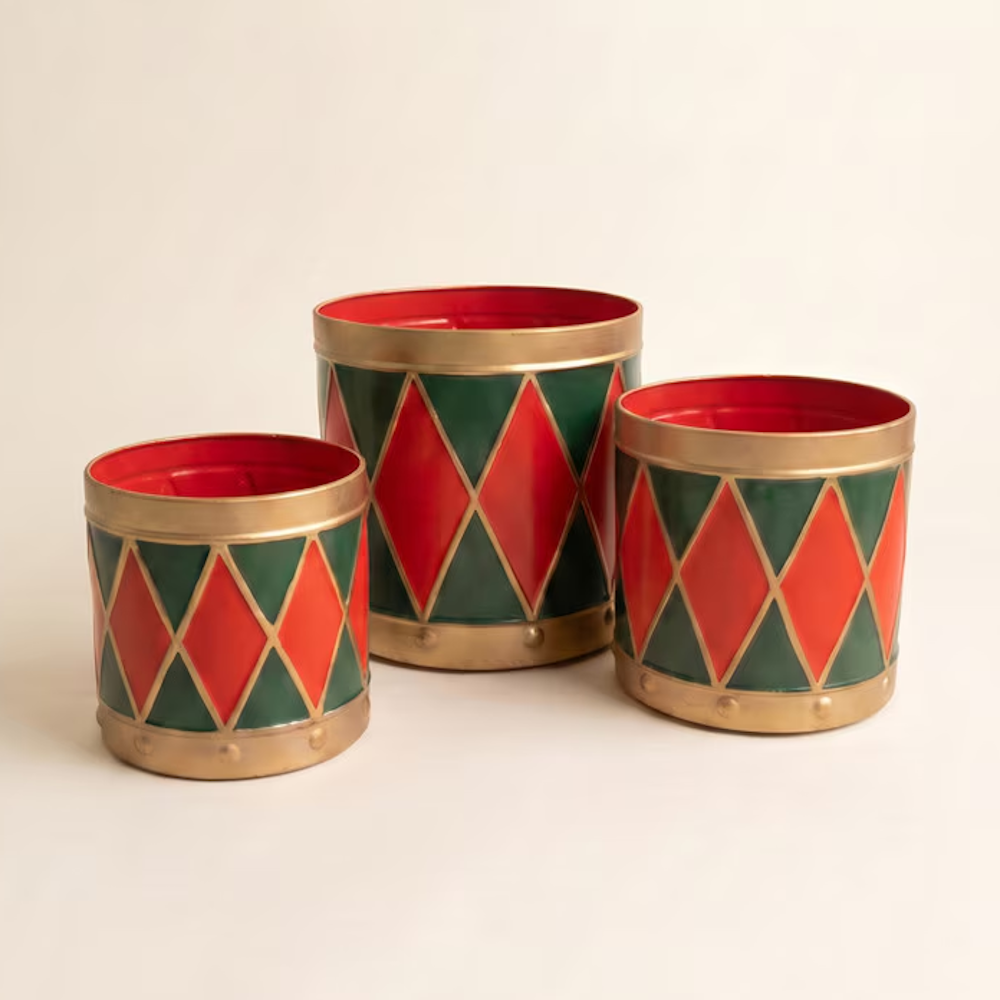 Three painted metal drum Christmas planters in graduating sizes with red and green harlequin patterns.