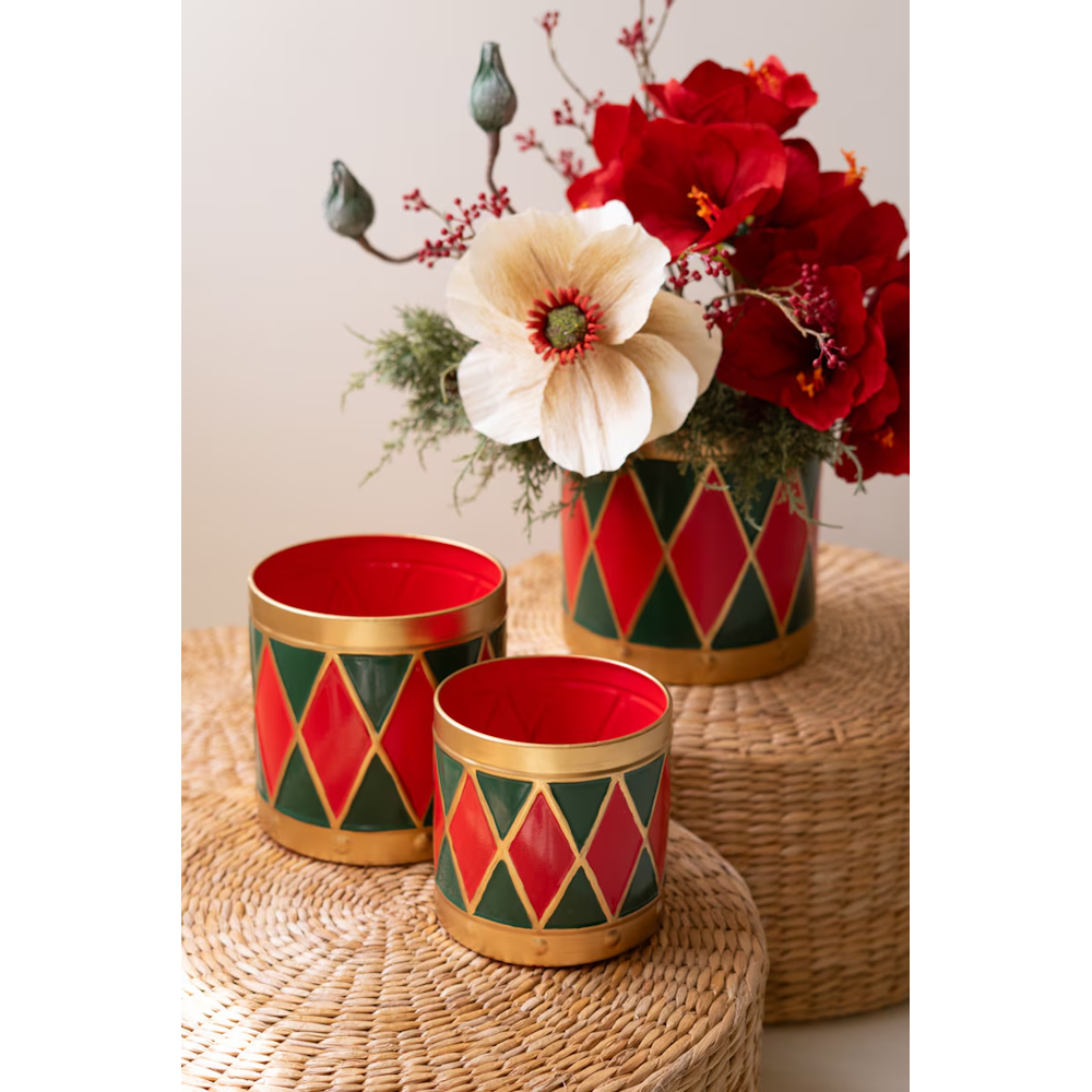 Three metal harlequin drum planters on woven stools, the largest holding floral sprigs.