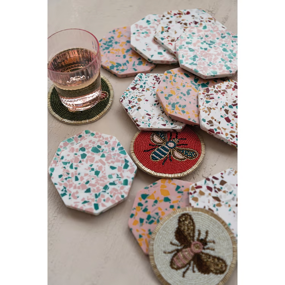 Beaded round coasters with bee designs and colorful hexagonal terrazzo coasters on a neutral tabletop.
