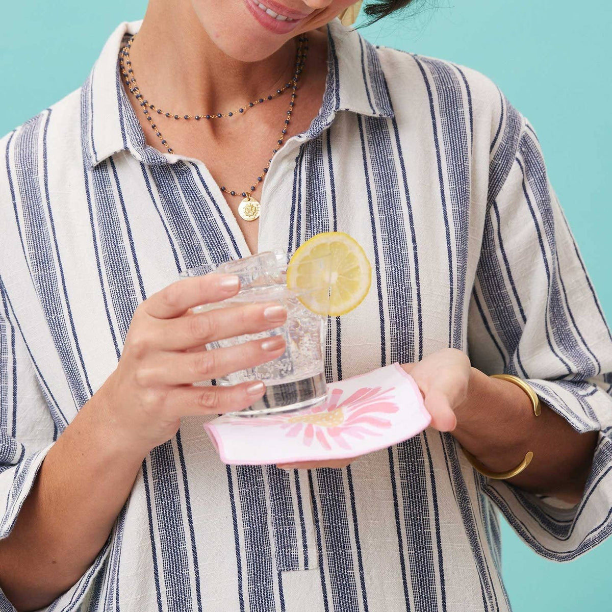Woman holding a cocktail with a lemon slice over a pink daisy cocktail napkin.