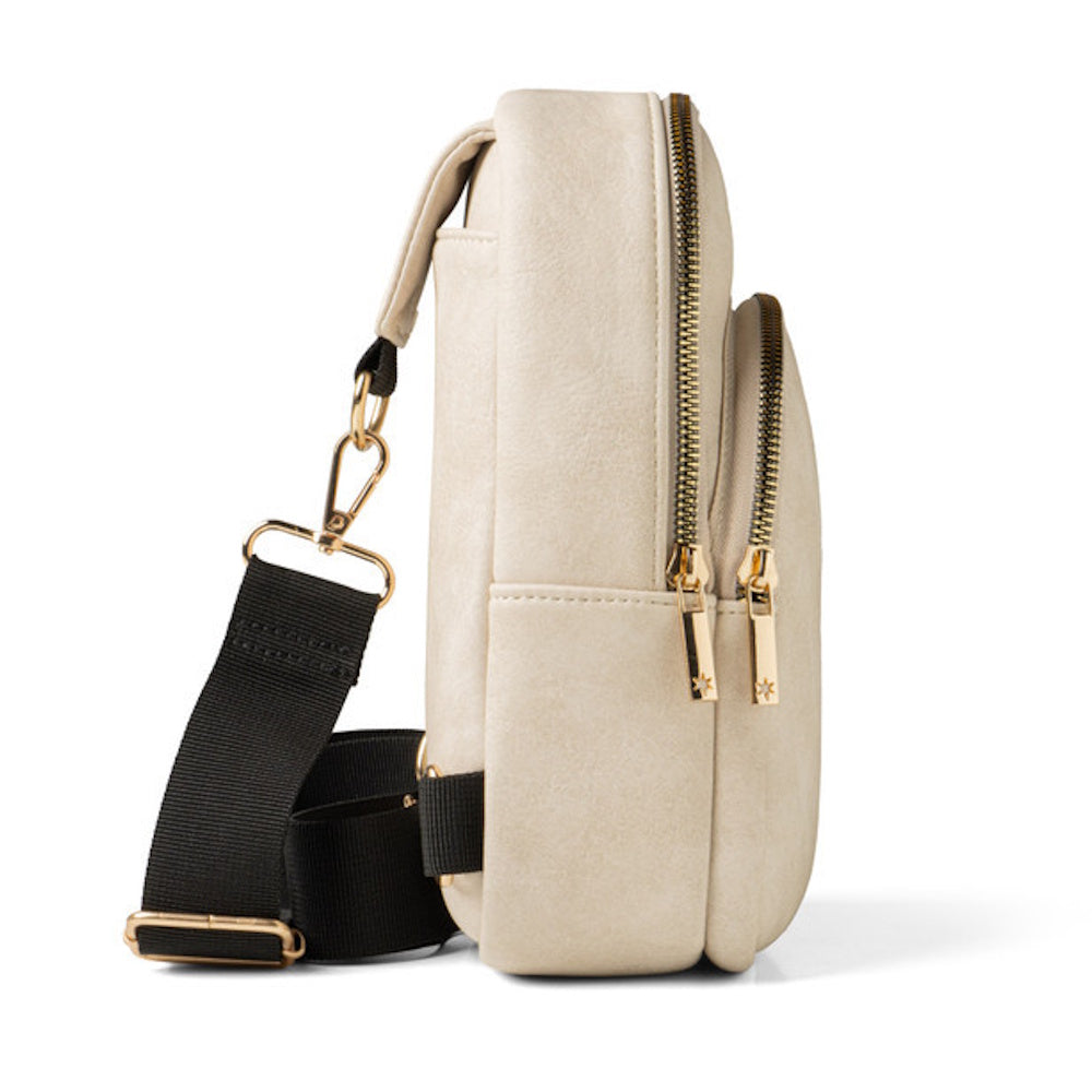 Side view of a beige faux leather sling bag with gold zippers and a black adjustable strap.