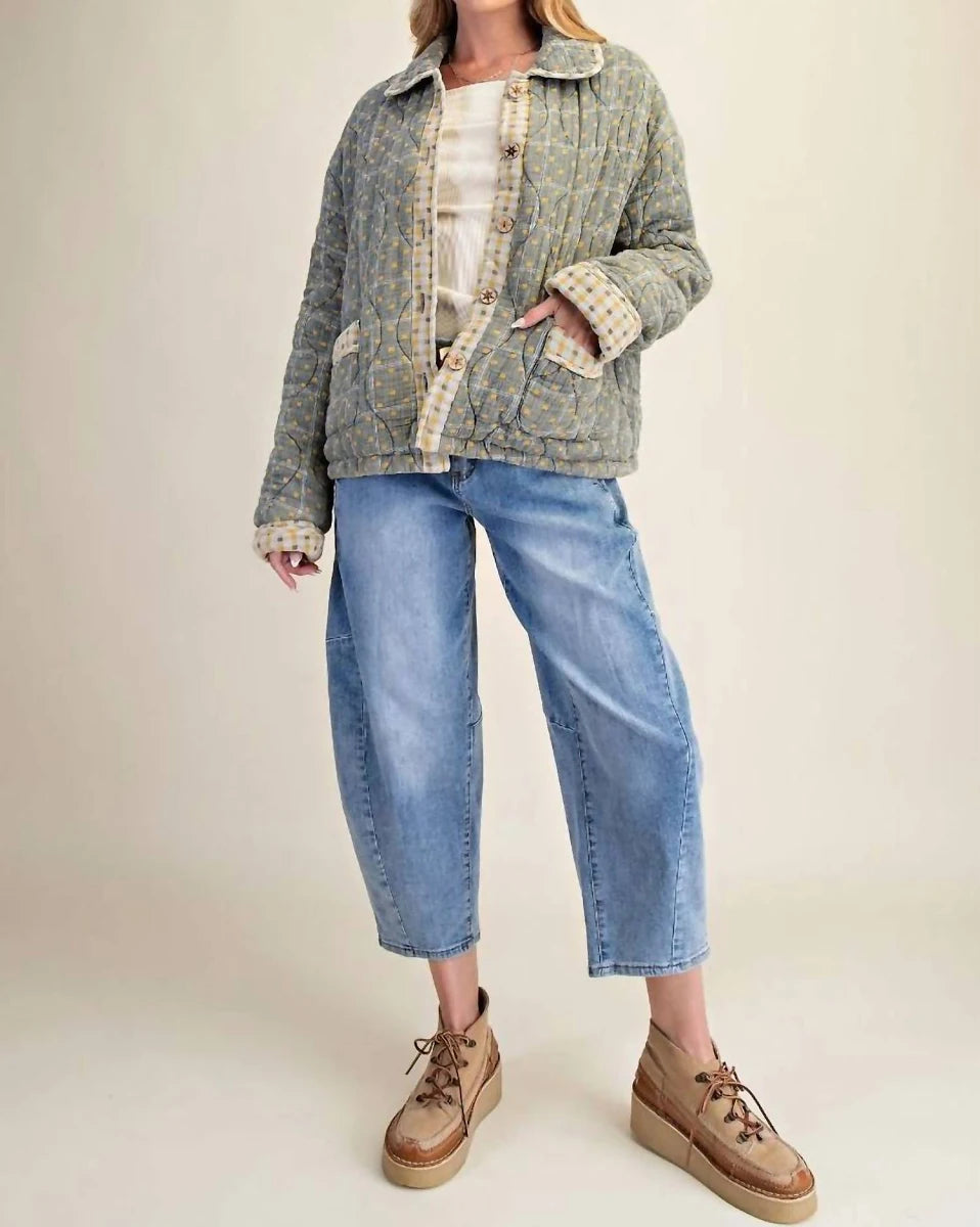 A model wearing a textured, patterned quilted jacket in muted green and beige tones, paired with light-wash cropped blue jeans and brown platform lace-up shoes, set against a plain beige studio background.