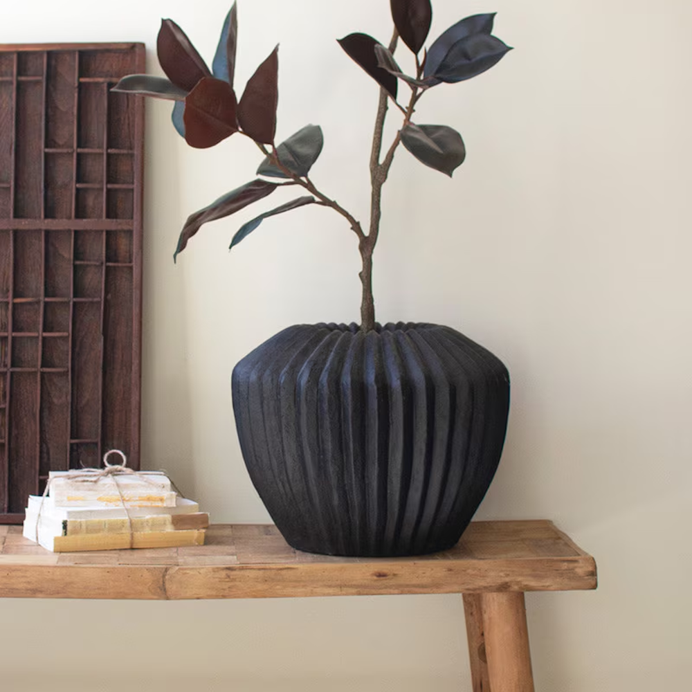 Black stone fluted composite urn with a leafy branch on a wooden bench.