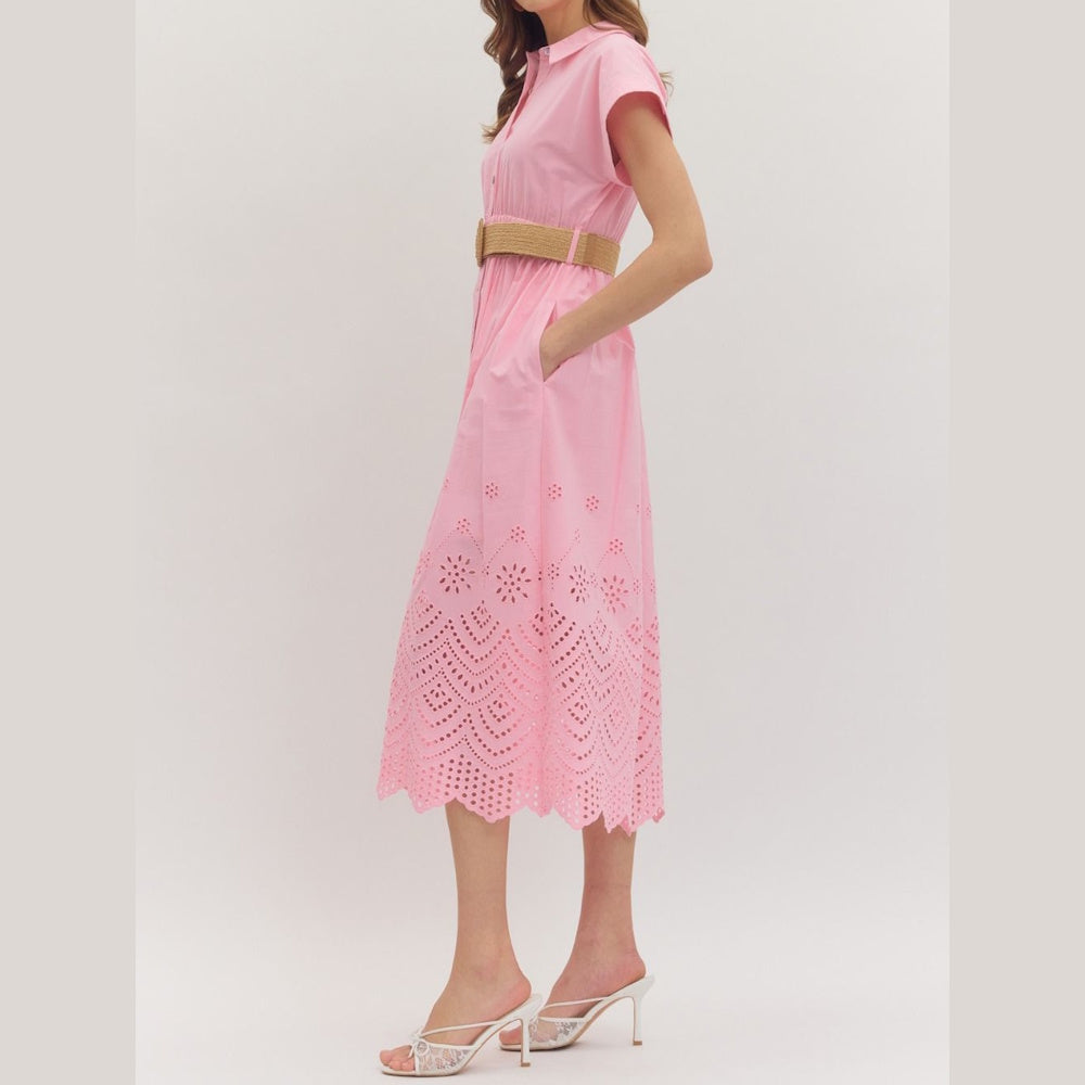 Side view of a pink eyelet midi shirtdress featuring a scalloped hem, straw belt, and pockets.