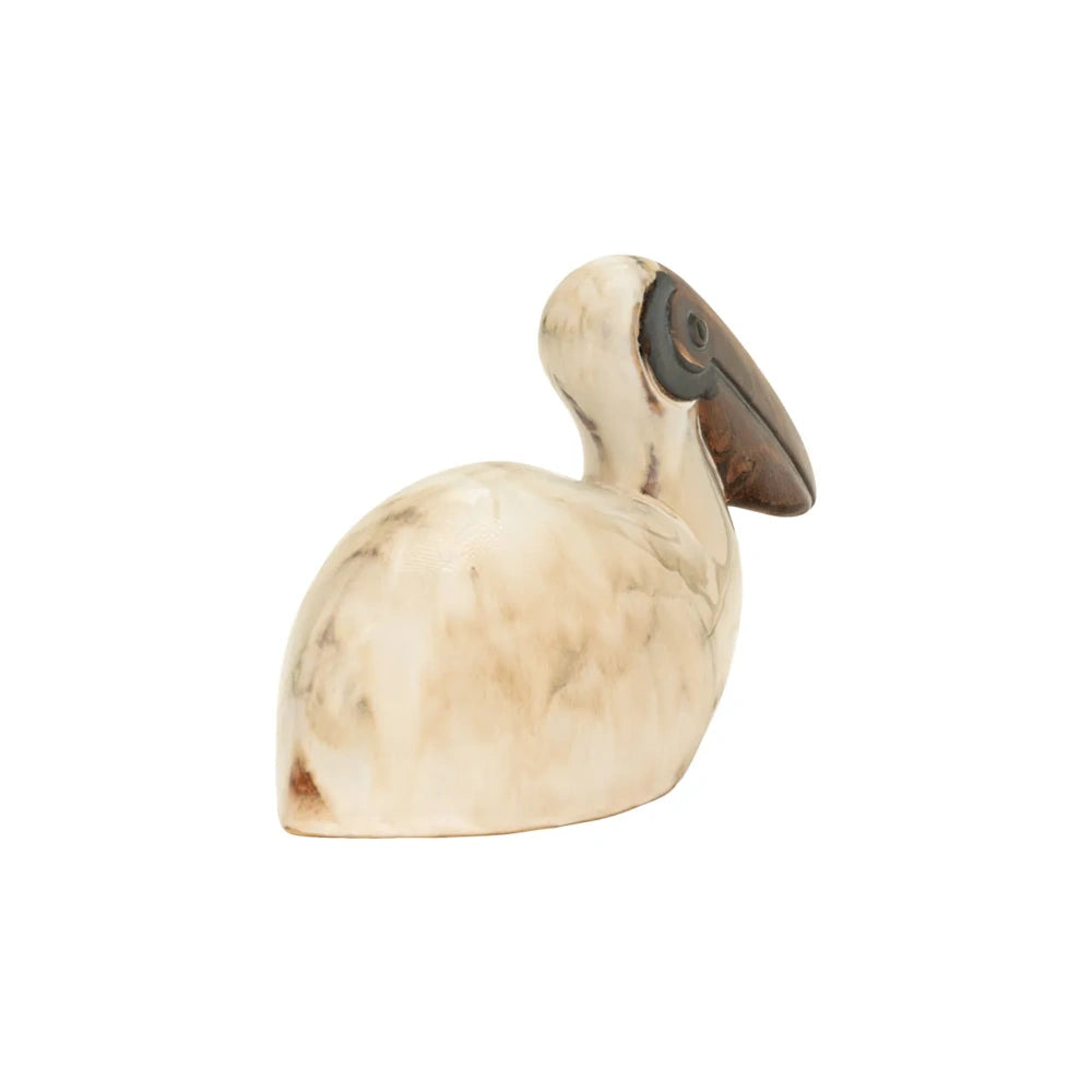 Rear side view of a small ceramic pelican figurine in marbleized off-white with a dark brown beak.
