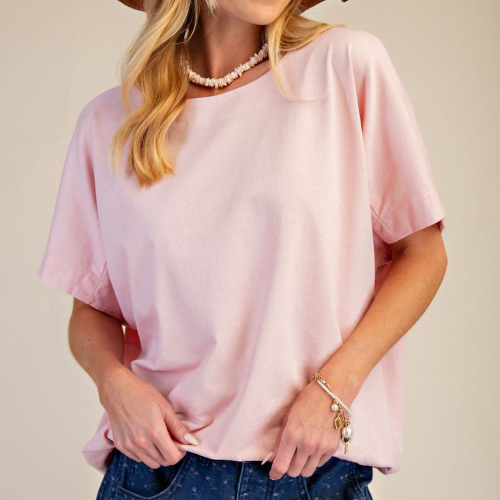 Woman wearing a light pink mineral wash boxy knit top with short sleeves and a round neckline.