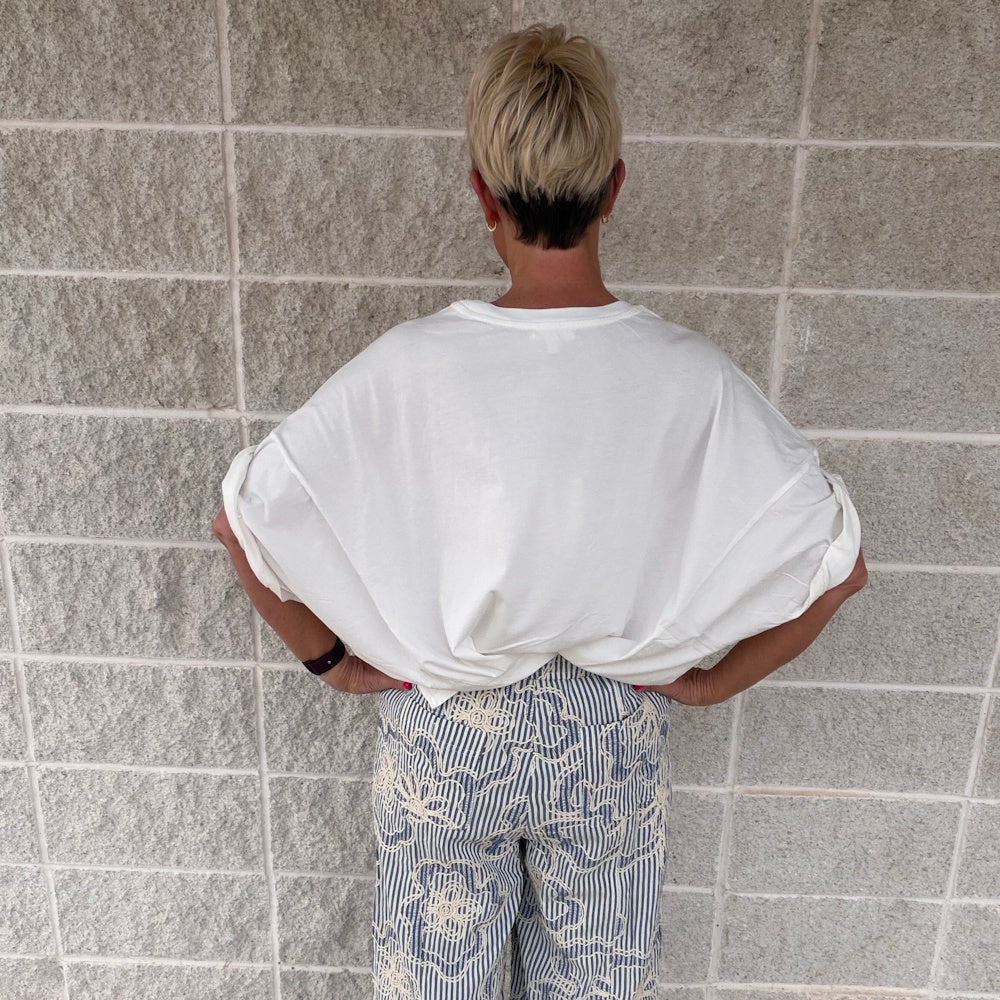 Back view of a woman with a blonde pixie cut wearing a white oversized t-shirt and blue striped patterned pants.