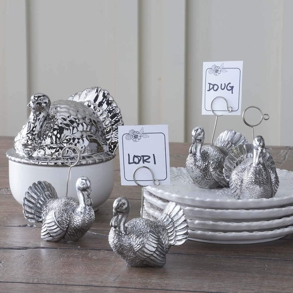 Silver turkey-shaped place card holders with handwritten name cards on a rustic wooden table.
