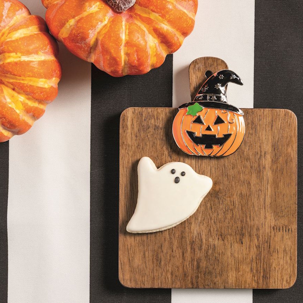 Halloween jack-o'-lantern charm and ghost cookie on a wooden serving board next to mini pumpkins.